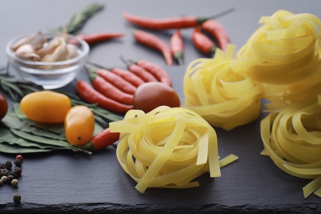 Pasta en la mesa con especias y verduras. Fideos con verduras para cocinar sobre un fondo de piedra negra.