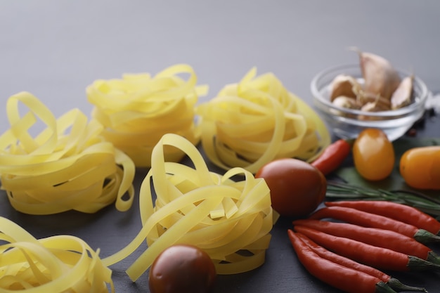 Pasta en la mesa con especias y verduras. Fideos con verduras para cocinar sobre un fondo de piedra negra.