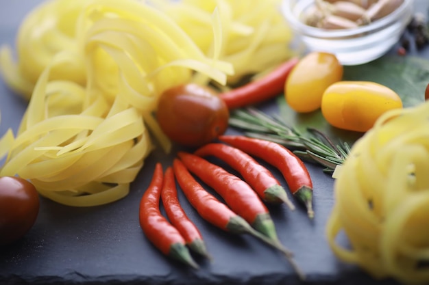 Pasta en la mesa con especias y verduras. Fideos con verduras para cocinar sobre un fondo de piedra negra.