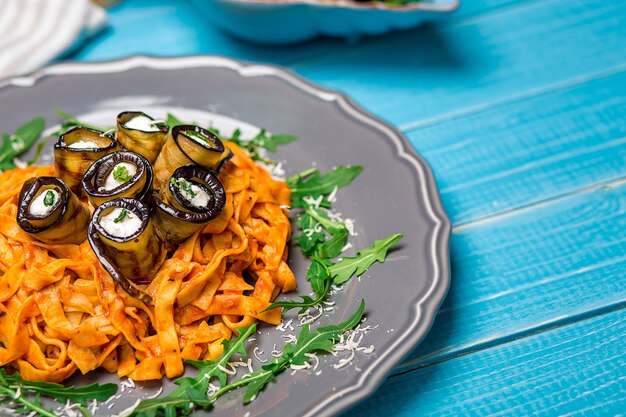 Pasta mit Auberginen, Tomaten, Käse und Rucola. Die originelle Präsentation des Gerichts vom Küchenchef. Auf einem blauen hölzernen Hintergrund.