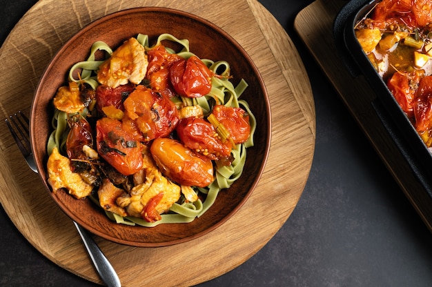 Pasta mit gebackenen Tomaten, auf einem runden Holzbrett und dunklem Hintergrund