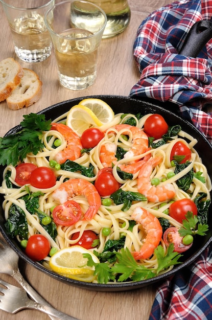 Pasta mit gebratenen Garnelen, Erbsen, Tomaten und Spinat in einer Bratpfanne auf einem Tisch mit Apfelglas