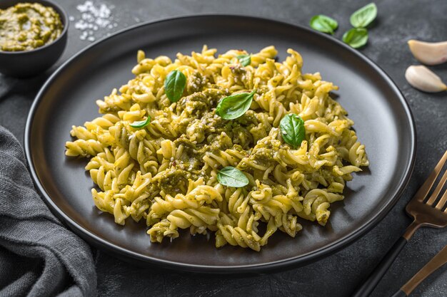 Pasta mit Pesto-Sauce, frischen Basilikumblättern und Sesamsamen auf dunklem Hintergrund