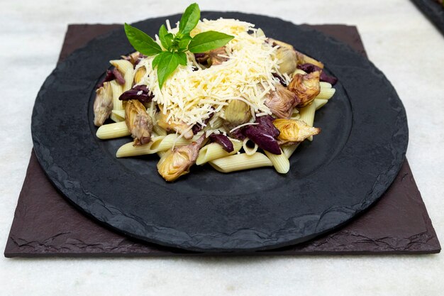 Pasta mit schwarzen Oliven, Parmesan, Artischockenherzen, garniert mit frischen Basilikumblättern.