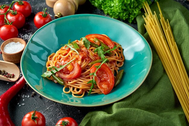 Pasta mit Tomaten, Spargel und roter Soße auf einem Teller auf dunklem Hintergrund