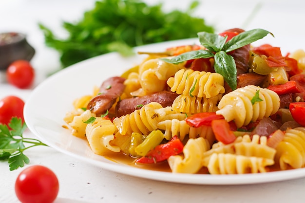 Pasta mit Tomatensauce mit Wurst, Tomaten, grünes Basilikum in weißen Teller auf einem hölzernen Hintergrund verziert.