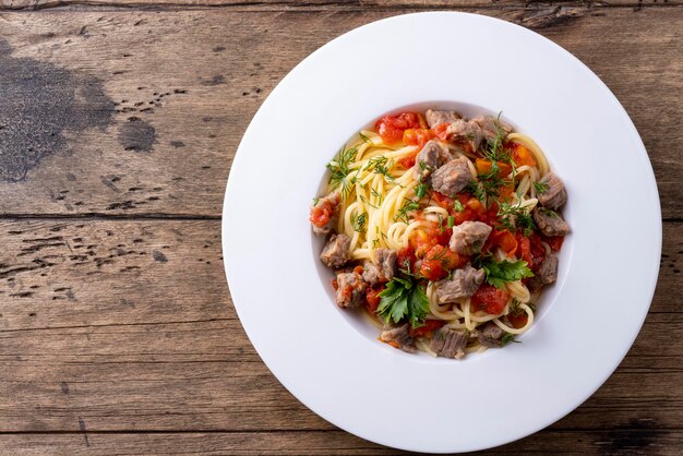 Pasta mit Tomatensauce und Fleisch auf weißem Teller und Holzhintergrund