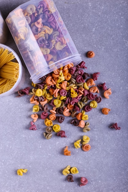 Pasta multicolor con la adición de colorante vegetal natural. Dispersos de una lata sobre una mesa de concreto