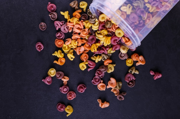 Pasta multicolor con la adición de colorante vegetal natural. Dispersos de una lata sobre una mesa de hormigón negro