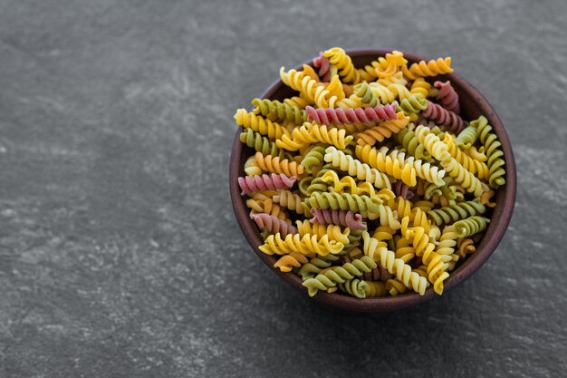 Pasta multicolor sin cocer en un tazón de madera sobre fondo blanco de madera