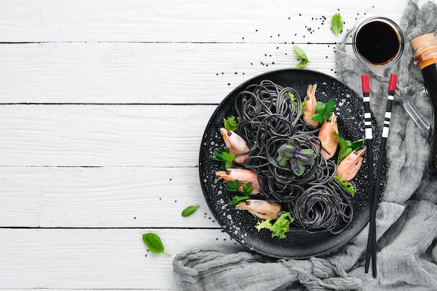 Pasta negra con gambas en un plato negro Vista superior Sobre un fondo de madera blanca Espacio de copia libre