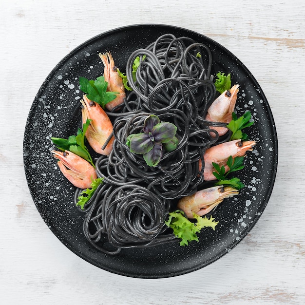 Pasta negra con gambas en un plato negro Vista superior Sobre un fondo de madera blanca Espacio de copia libre