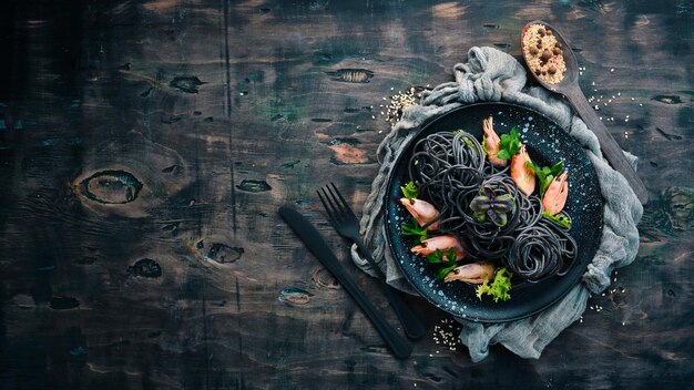 Pasta negra con gambas en un plato negro. Vista superior. Sobre un fondo negro. Espacio de copia libre.