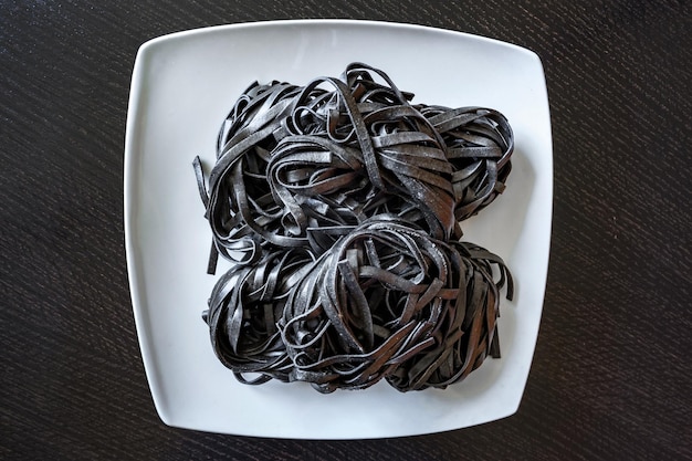 Foto pasta negra seca con tinta de sepia pasta de sémola de trigo duro con tinta de calamar en un plato cuadrado