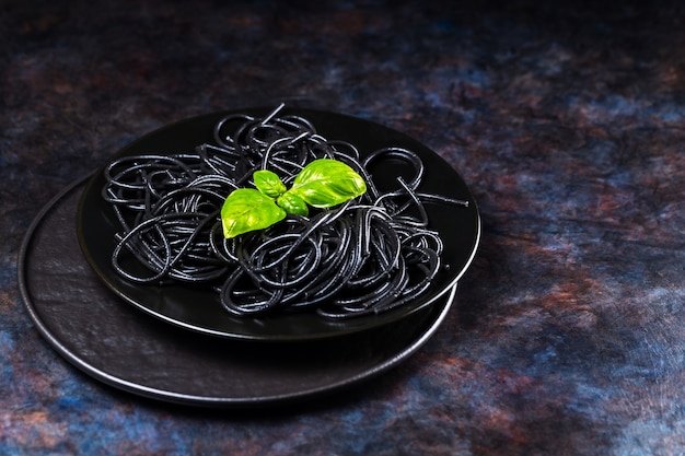 Pasta negra tinta de sepia con salsa pesto y albahaca fresca. Espaguetis negros con hojas de albahaca en plato negro. Fondo oscuro