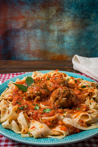 Pasta o Fettuccine con salsa de tomate y albóndigas en un plato rústico sobre un mantel a cuadros.