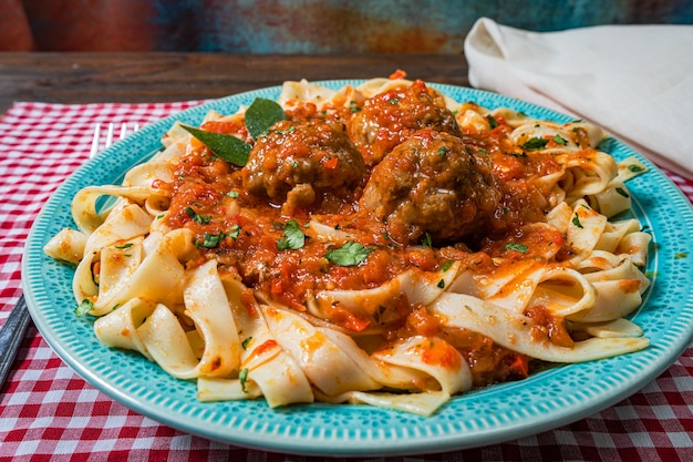 Pasta oder Fettuccine mit Tomatensauce und Fleischbällchen in einem rustikalen Teller auf einer karierten Tischdecke.