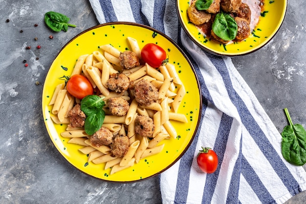 Pasta penne con albóndigas y salsa de tomate sobre una placa amarilla y una superficie gris