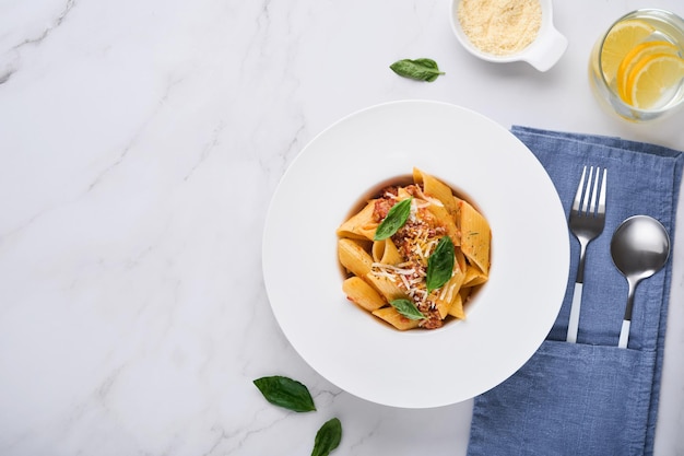 Pasta penne a la boloñesa. Sabrosa y apetitosa pasta penne italiana clásica con queso parmesano, albahaca y salsa boloñesa en un plato blanco sobre un plato sobre una mesa de piedra Plato tradicional de la cocina italiana. Vista superior