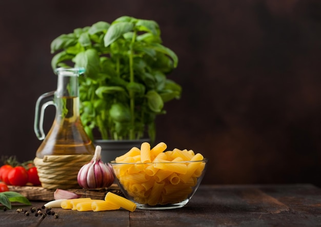 Pasta penne cruda fresca en recipiente de vidrio con aceite vegetal de albahaca y tomates con ajo