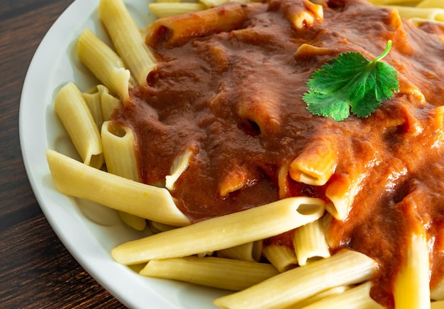 Pasta penne italiana típica sobre fondo de madera con salsa de tomate