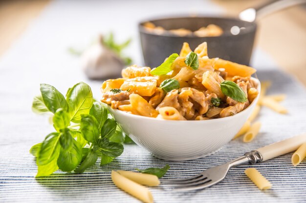 Pasta Penne mit Hühnchenstücken, Pilzen, Basilikum und Parmesan, italienisches Essen in einer weißen Schüssel auf dem Küchentisch.