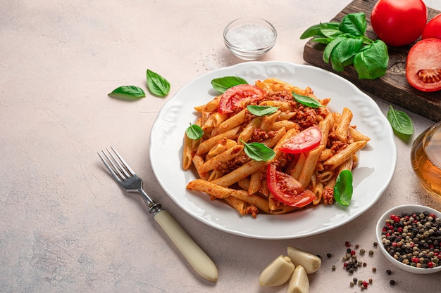 Pasta penne con salsa boloñesa, un plato tradicional italiano sobre un fondo claro. Vista lateral, copie el espacio.