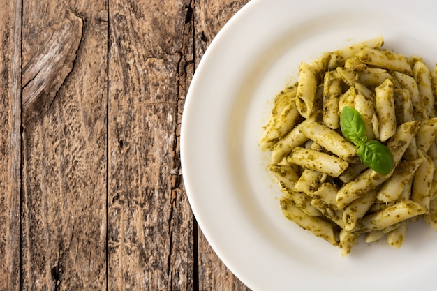 Pasta penne con salsa pesto sobre mesa de madera