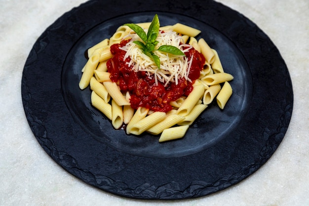 Pasta penne con salsa roja y queso parmesano en una placa negra. Fondo de piedra u hormigón