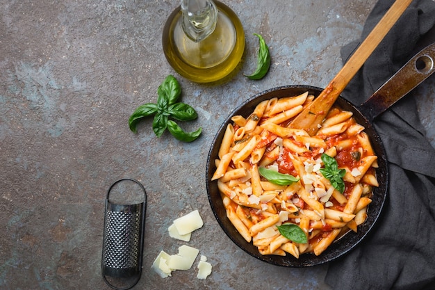 Pasta penne en salsa de tomate y queso decorada con albahaca sobre piedra gris