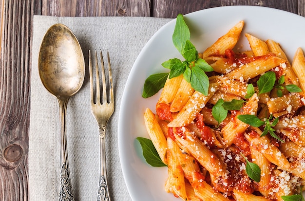 Pasta penne en salsa de tomate con queso parmesano de albahaca sobre mesa de madera rústica.