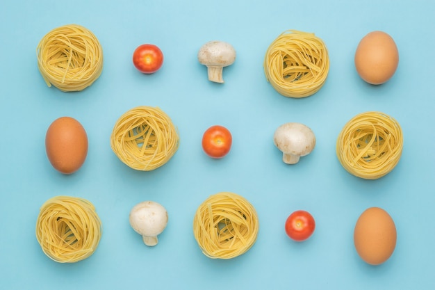 Pasta, Pilze, Eier und Tomaten auf einer blauen Oberfläche. Zutaten für die Herstellung von Nudeln.