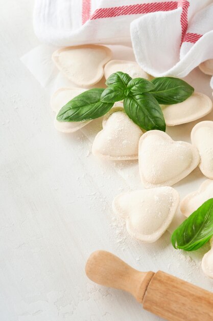 Pasta de ravioles italianos en forma de corazón Sabrosos ravioles crudos con harina y albahaca sobre fondo blanco Fondo de ingredientes para cocinar San Valentín o ideas para el almuerzo del Día de la Madre Vista superior con espacio para copiar