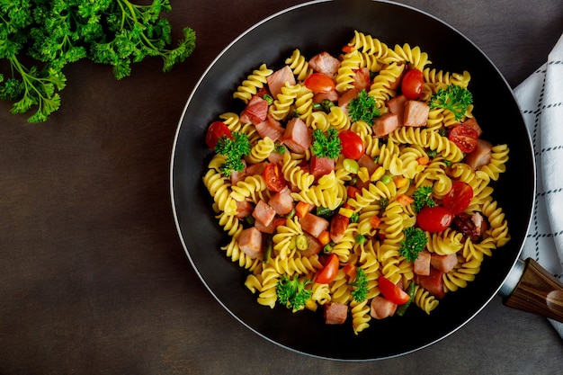 Pasta rotini con guisantes, jamón y perejil en sartén. Cocina italiana.