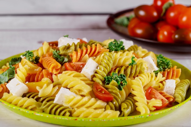 Pasta rotini y tomate cherry con ensalada verde en mesa de madera