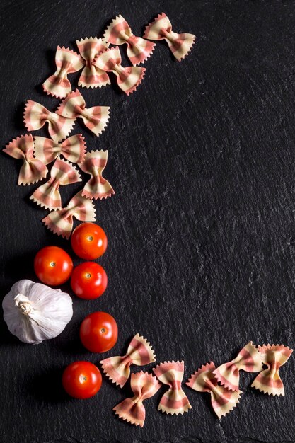 Pasta Schmetterlinge, Tomaten und Knoblauch auf schwarzem Schiefer