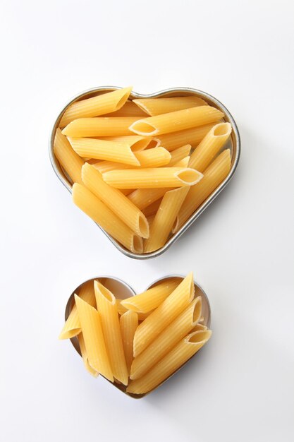 Foto pasta seca de penne en el recipiente en forma de corazón