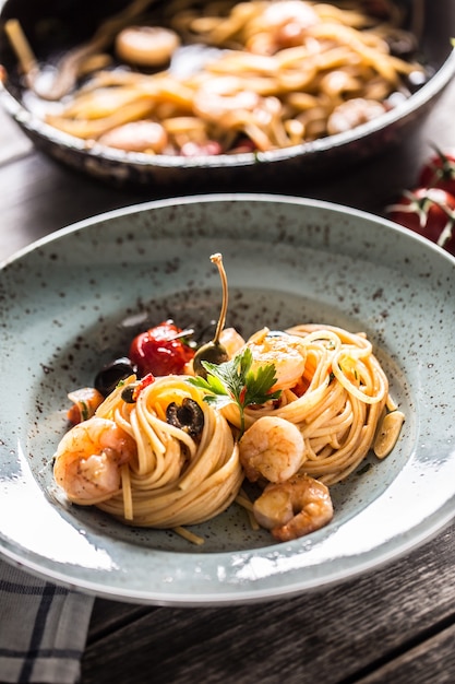 Pasta Spaghetti auf Teller und Pfanne mit Garnelen Tomatensauce Tomaten und Kräutern. Italienische oder mediterrane Küche.