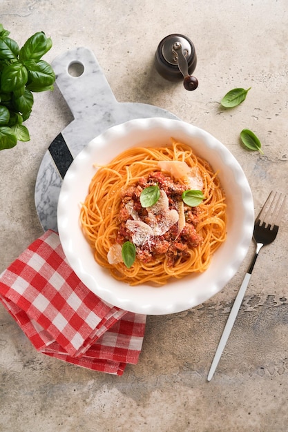 Pasta Spaghetti Bolognese Leckere appetitanregende italienische Spaghetti mit Bolognese-Sauce Tomatensauce Käse Parmesan und Basilikum auf weißem Teller auf grauem Stein oder Betontisch Hintergrund Ansicht von oben