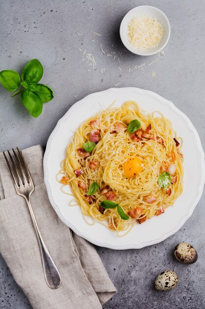 Pasta Spaghetti Carbonara mit Speck, Parmesan, Eigelb und Basilikumblättern auf grauer heller Oberfläche. Traditionelles italienisches Gericht