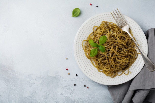 Pasta Spaghetti mit Pesto-Sauce, Basilikum und Parmesan auf einer weißen Keramikplatte und grauer Beton- oder Steinoberfläche. Traditionelles italienisches Gericht. Selektiver Fokus. Draufsicht.