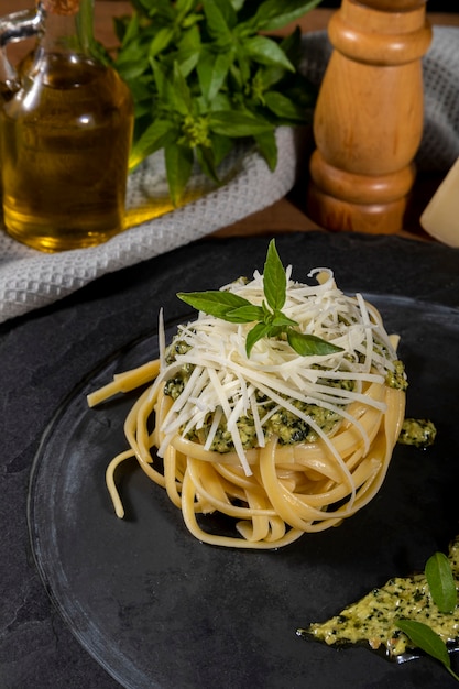 Pasta Spaghetti mit Pesto-Sauce und frischen Basilikumblättern in schwarzer Steinschale auf Holzhintergrund.