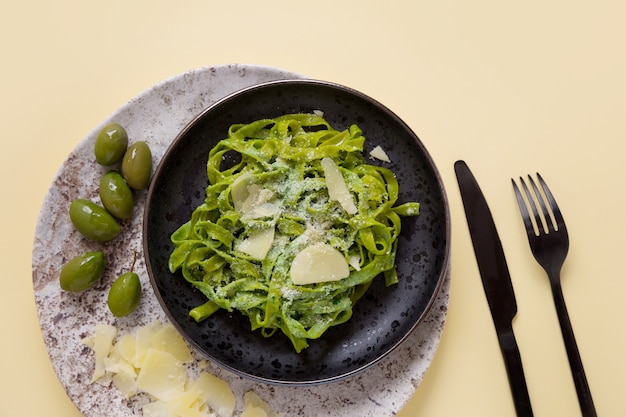 Pasta de tagliatelle de espinacas con salsa, aderezada con queso sobre una superficie de color amarillo. Pasta verde