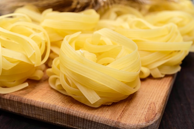 Pasta-Tagliatelle in Form von Nestern auf dem hölzernen Hintergrund. Nahansicht.