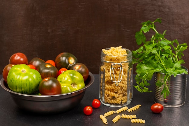 Pasta en tarro de cristal ramitas de perejil en tarro de metal y tomates en cuenco de metal