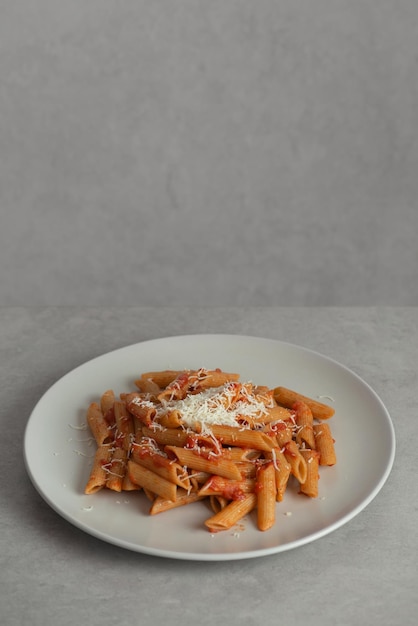 Pasta en un tenedor con tomates y queso en un plato sobre un fondo gris