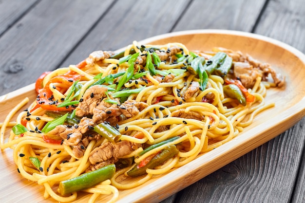 Pasta con ternera y verduras sobre un fondo de madera en una placa de bambú