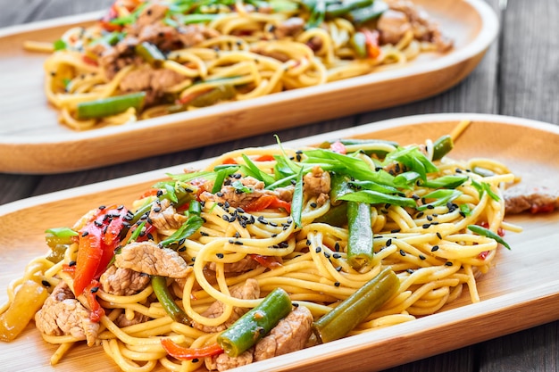 Pasta con ternera y verduras sobre un fondo de madera en una placa de bambú