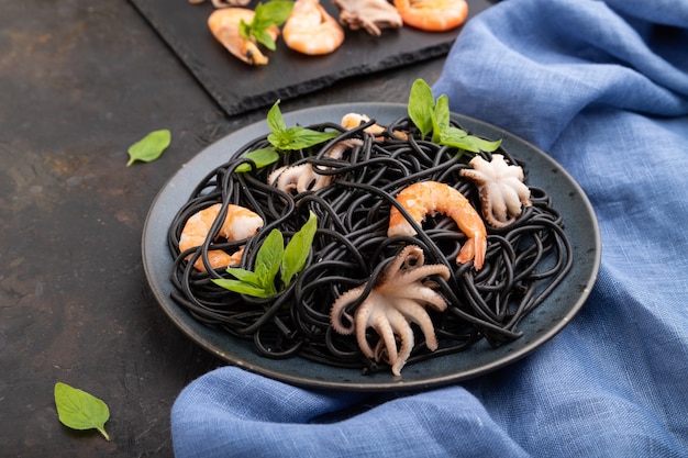 Pasta de tinta de sepia negra con camarones o gambas y pequeños pulpos sobre superficie de hormigón negro y textil azul