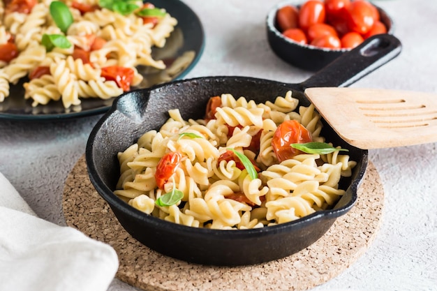 Pasta con tomate y albahaca en una sartén y en un plato y un bol con tomates en la mesa Cocina mediterránea